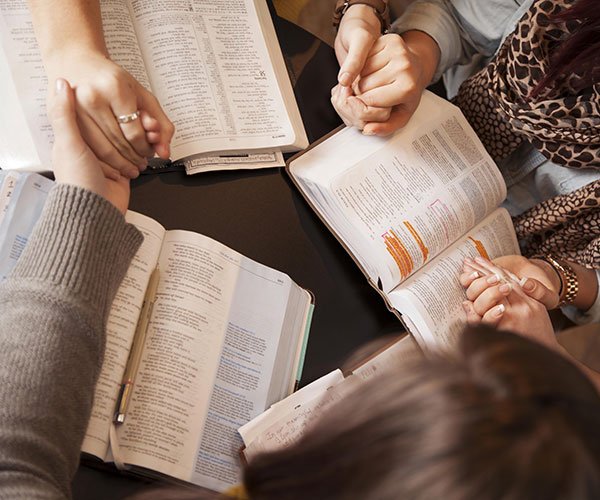 People gathered around a table, holding hands, and praying over the word of the bible.
